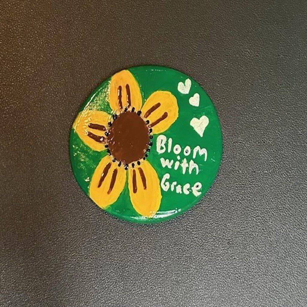 Painted sunflower rock with "Bloom with Grace.