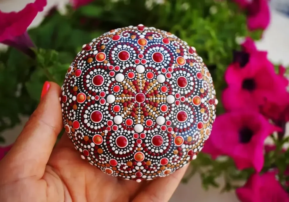 Hand holding a colorful mandala stone outdoors.